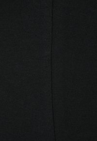 Gros plan sur un tissu noir avec une couture centrale verticale, montrant une texture fine en maille des deux côtés.