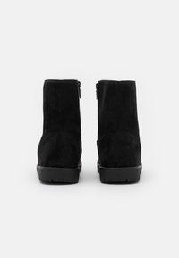 Bottines en suède noir avec une texture lisse, dotées de fermetures éclair sur les côtés et de semelles en caoutchouc plates. Le design est simple et épuré.