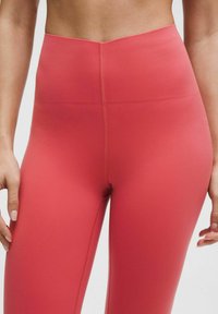 Leggings cu talie înaltă de culoare coral roz, fabricate dintr-un material elastic. Prezintă o textură netedă și cusături plate pentru confort. Fără modele vizibile.