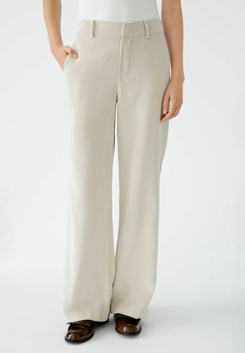 Pantalones de pierna ancha color crema con textura de canalé vertical, que cuentan con bolsillos laterales y una cinturilla estructurada.