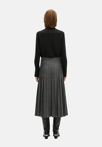 Haut à manches longues noir associé à une jupe maxi plissée en plaid gris. La jupe présente des plis verticaux et est portée avec des bottes à talons noires.