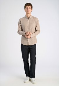 Camicetta a maniche lunghe a righe marrone chiaro con colletto button-down e tasca, abbinata a pantaloni blu navy e sneakers bianche.