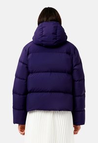 Jachetă pufoasă purpurie cu glugă, cu secțiuni late și orizontale quilted și manșete elastice, având o textură netedă și lucioasă.
