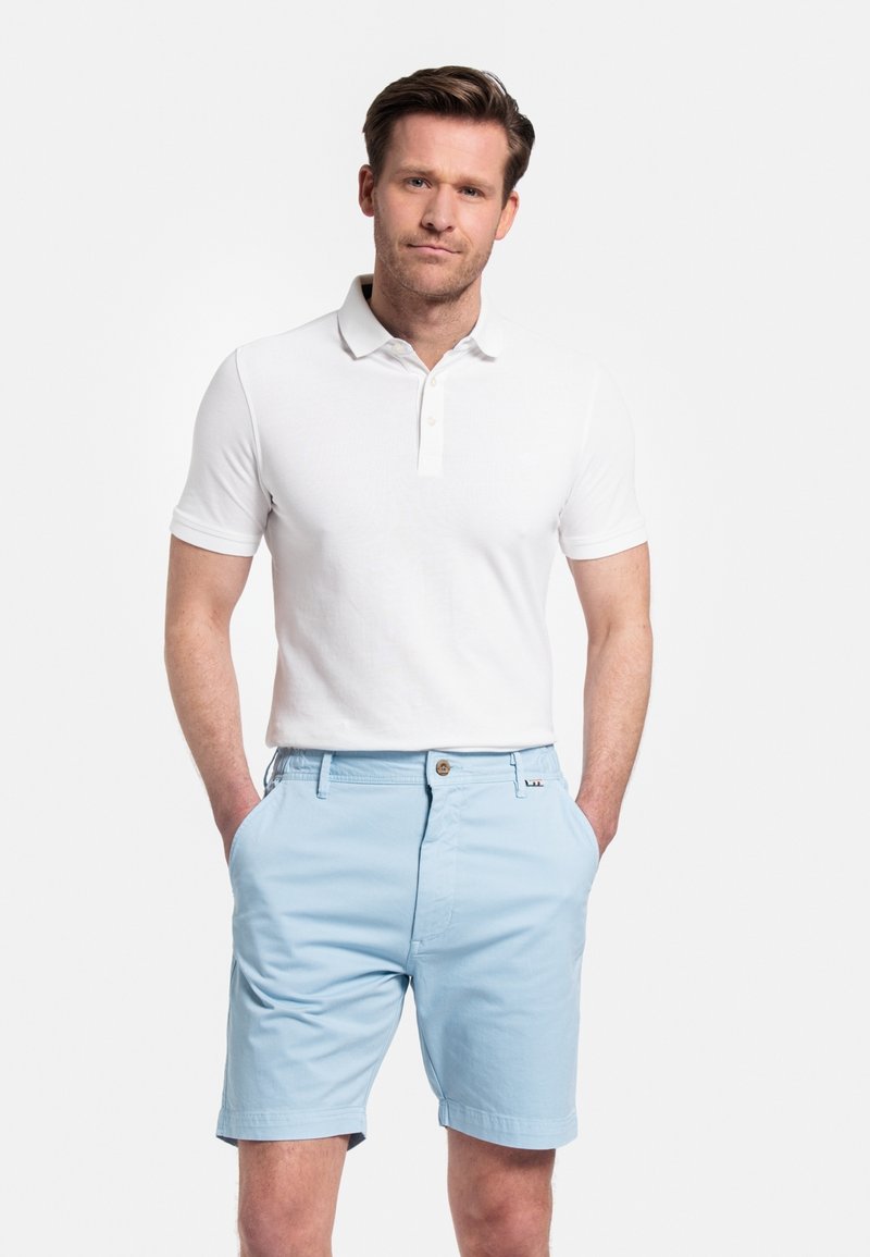 Witte polo met korte mouwen en twee knopen, gecombineerd met lichtblauwe shorts met een knoopsluiting en zijzakken.