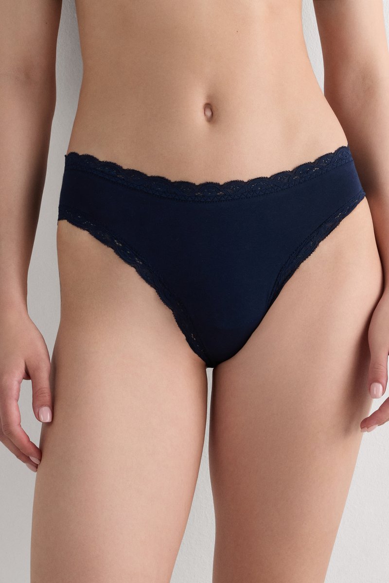 Mujer vestida con bikini azul marino con encaje, de pie contra un fondo blanco liso.
