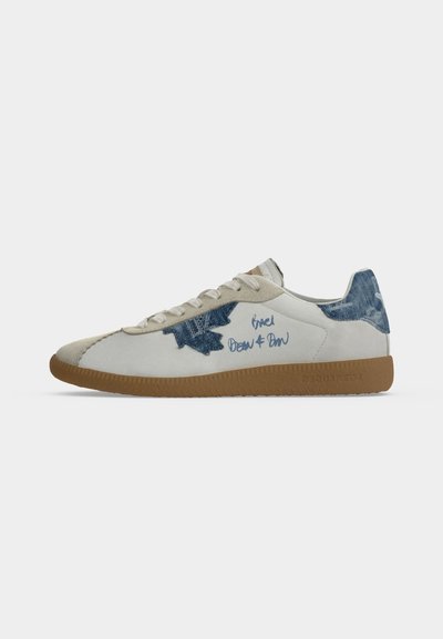 Baskets blanches avec semelle en gomme, patches en denim sur le côté et le talon, lacets beiges et texte manuscrit bleu sur le côté extérieur.