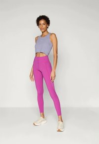 Világos lila, rövidített felső, amelyet magas derekú, szűk pink leggingsekkel viselnek. Az öltözet rugalmas sportanyagból készült.