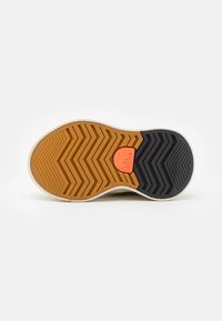 Gummisula med ett zigzag-mönster; har detaljer i orange och kontrasterande svarta och bruna sektioner. Slät textur, rundad form.