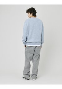 Pull en maille bleu clair avec un col rond, associé à un pantalon gris ample. Texture en laine mérinos, coupe décontractée, avec des poches à l'arrière.