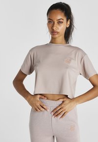 Vaaleanpunainen lyhythihainen cropped t-paita, jossa on pyöreä kaula-aukko ja brodeerattu logo rinnassa, yhdistettynä vastaaviin teksturoituihin housuihin.