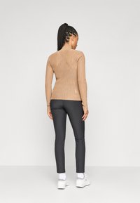 Hnedý rebrovaný top s dlhým rukávom a priliehavým strihom, skombinovaný s čiernymi úzkymi nohavicami a bielymi teniskami. Zadný pohľad zvýrazňuje textúrovanú tkaninu.