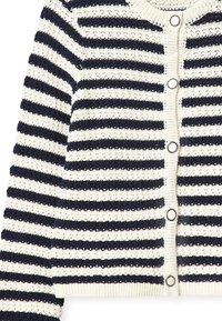 Virkat kofta med mörkblå och krämfärgade horisontella ränder, med stora metallknappar och ribbad nederkant. Öppenstickad textur.