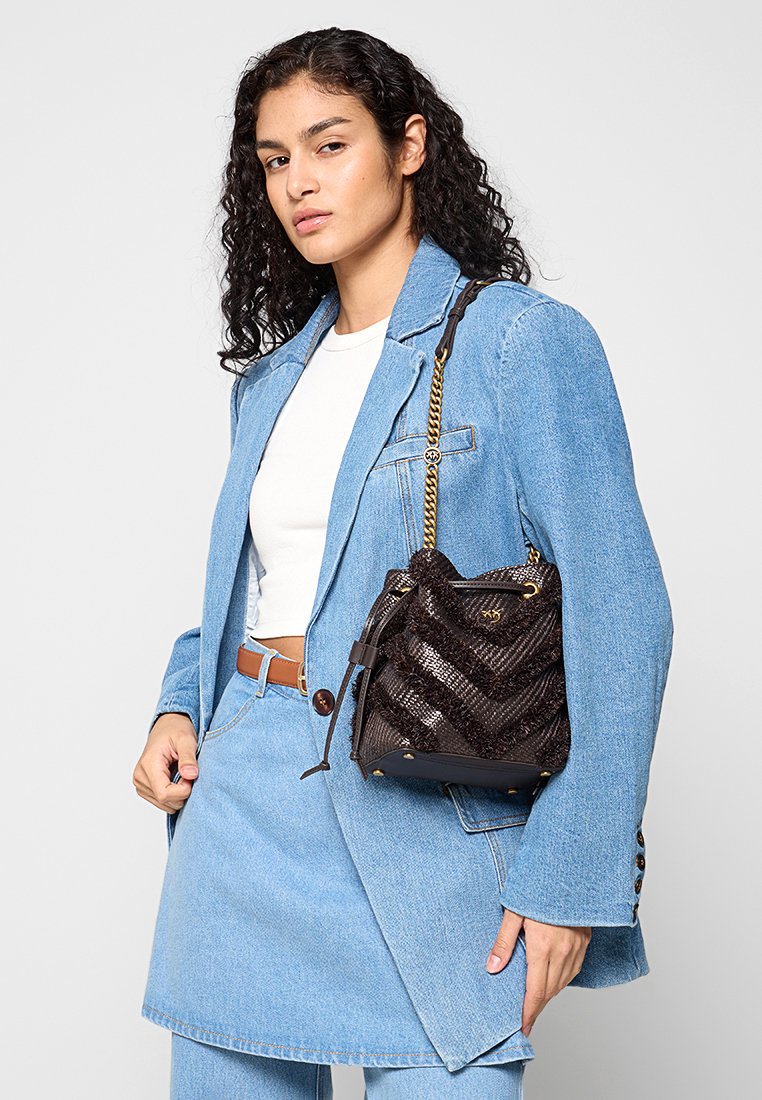 Czarna torebka teksturowana w wzór chevron z złotym łańcuchem, trzymana przez osobę w niebieskim dżinsowym stroju z białą bluzką.