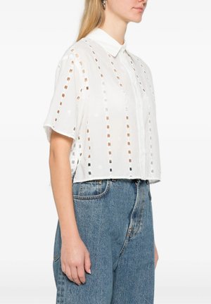 Donna con camicia bianca a maniche corte con strisce verticali traforate e jeans blu a vita alta.