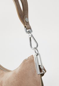 Sezione della borsa in suede beige con una chiusura metallica argentata e una tracolla removibile. Presenta una zip liscia e una superficie morbida e texture.
