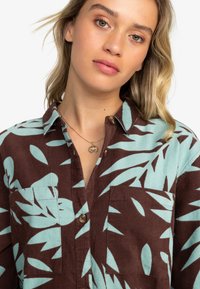 Brown corduroy shirt with light blue leaf pattern, featuring a button placket and chest pocket, textured fabric, and collar.