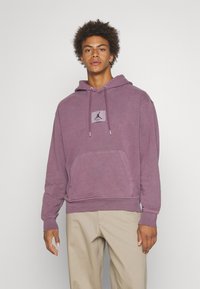 Sudadera morada de tela suave, con un bolsillo frontal y un parche con el logo en el pecho. El diseño incluye una capucha con cordón.