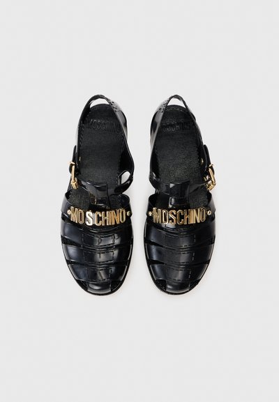 Mustad plastikust sandaalid, millel on ristiühtlusdisain, esiküljel on kuldne "MOSCHINO" logo ja reguleeritav pahkluuring.