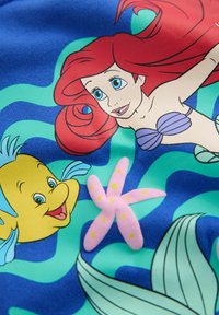 Tissu coloré présentant des personnages de sirène et de poisson sur un fond bleu avec des motifs ondulés verts. Comprend un détail d'étoile de mer rose.