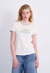 Kremo spalvos trumpas rankovės marškinėliai su žalia apdaila, papuošti gėlių motyvais ir „new balance“ grafika. Minkšta medvilnės medžiaga. Atsitiktinis siluetas.
