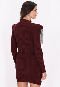 Bordeaux geribbelde sweaterjurk met lange mouwen, slank ontwerp en franje-details op de schouders, vervaardigd uit een textuurstof met een lichte stretch.