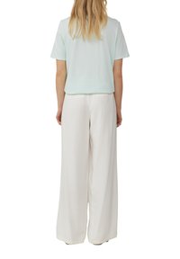 Lichtblauw korte mouwen top gecombineerd met witte wijde broek. De top heeft een relaxte pasvorm; de broek heeft een gladde, vloeiende stof.