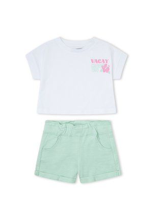 Camiseta blanca de manga corta y corte corto con "VACAY MODE ON" y hibisco rosa, combinada con pantalones cortos de dobladillo enrollado en verde menta con cintura elástica y bolsillos.