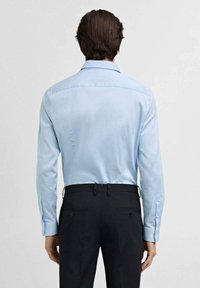 Chemise bleu clair à manches longues avec une texture douce et des poignets boutonnés, assortie à un pantalon noir bien ajusté avec des poches arrière et des boutons.