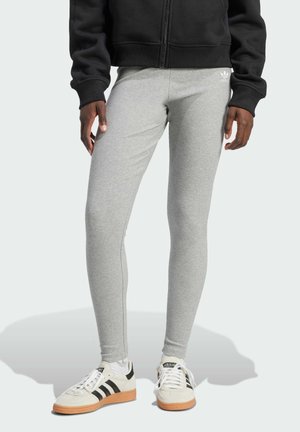 Leggings grigi realizzati in materiale elasticizzato, con una texture liscia e una vestibilità slim, abbinati a sneaker nere e bianche.