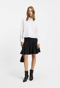 White cropped shirt with buttons and a collar, paired with a black flared skirt. Black ankle boots with pointed toes and decorative hardware.