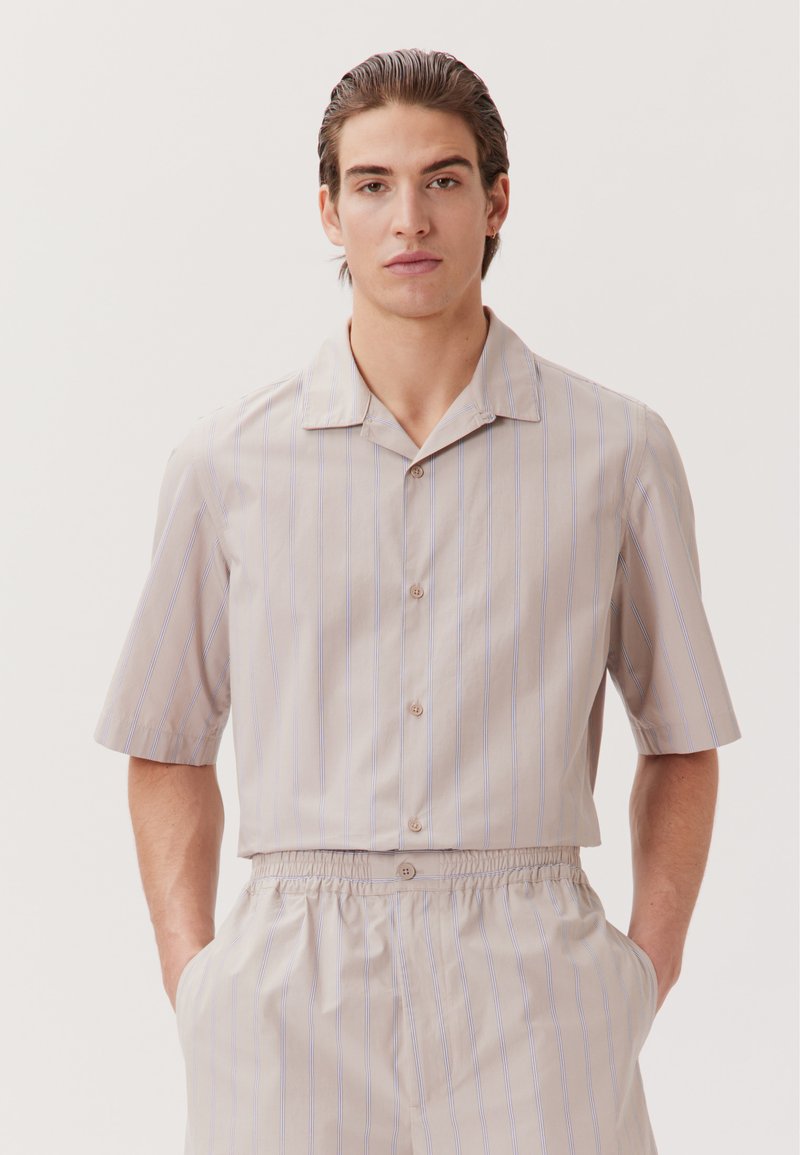 Chemise à manches courtes, col en beige clair avec des rayures verticales bleues. Elle possède une fermeture boutonnée à l'avant et une coupe décontractée. Texture lisse.
