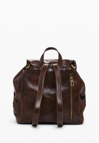 Pruun nahast seljakott, millel on kaks õlarihma, ülemine käepide, esine lukkude tasku ja sile tekstuur. Omab kuldset metallist aksessuaari.