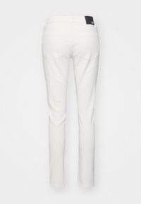 Vaqueros blancos de corte slim, con bolsillos traseros y una etiqueta de marca negra. La tela parece lisa con un leve brillo.