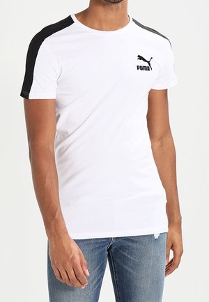 T-shirt blanc à manches courtes avec des panneaux noirs sur les épaules. Présente un petit logo Puma noir sur la poitrine. Le tissu semble lisse et léger.