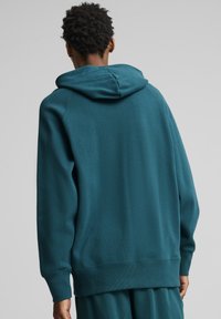 Felpa teal con cappuccio, polsini e orlo a coste. Realizzata in tessuto testurizzato, presenta una vestibilità comoda e elementi di design minimali.