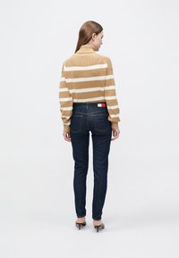 Csíkos barna és krémszínű garbó pulóver sötétkék skinny farmerral párosítva. Figyelemre méltó részletek közé tartozik egy címke a farmeren és a tűsarkú cipők.