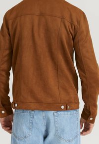 Chaqueta de ante marrón con una textura suave, de corte recto, con costuras visibles y detalles de presión en la cintura y los puños.