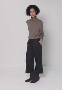 Pull à col roulé marron associé à un pantalon large à fines rayures sombres et des bottines foncées, offrant une tenue élégante et minimaliste.