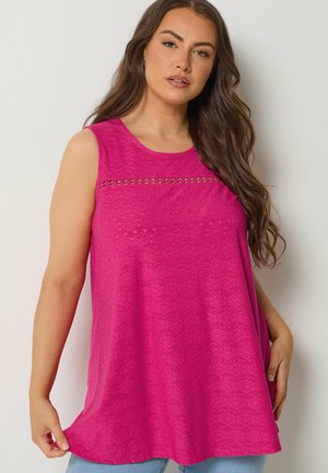 Donna con capelli lunghi castani che indossa una maglietta senza maniche rosa acceso con motivi floreali e dettaglio di pizzo orizzontale sul petto.