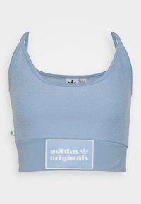 Světle modrý tílko s texturovanou horní částí, hladkou dolní sekcí a bílým logem "adidas originals" na obdélníkovém štítku. Nastavitelné ramínka.