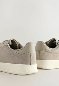 Lys grå ruskinds sneakers med gummisåler, der har diskrete sømdetaljer og en tekstureret finish på hælen og sidepanelerne.