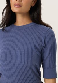 Knitted blue top with a ribbed texture, crew neckline, and elbow-length sleeves. The fabric appears soft and lightweight.