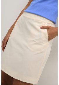 Béžová sukně s hladkou texturou, s dobře padnoucím pasem a boční kapsou. Lem je rovně střižený, což zdůrazňuje její minimalistický design.