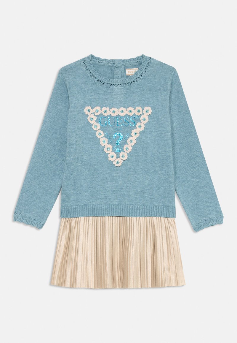 Suéter azul de malha com um triângulo decorativo de apliques florais e lantejoulas, combinado com uma saia dourada plissada. Decote redondo, mangas longas.