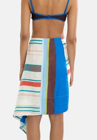 Wielokolorowa lniana spódnica z pionowymi paskami w kolorach niebieskim, brązowym, zielonym, czerwonym i białym; asymetryczny dół i gładka tekstura.