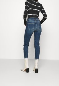 Jeans de mezclilla azul de tiro alto con pierna estrecha y acabado desgastado. Combinados con una camiseta de rayas en blanco y negro de manga larga y botas de tacón blancas.