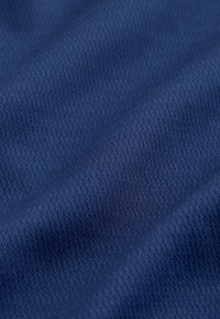 Gros plan sur un tissu texturé bleu foncé avec un motif en zigzag fin et répétitif et des plis doux.