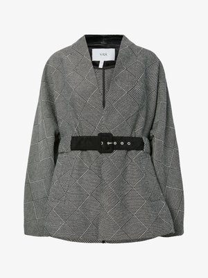 Veste à motifs noir et blanc avec un design géométrique, dotée d'un col montant, de manches longues et d'une ceinture noire à la taille.