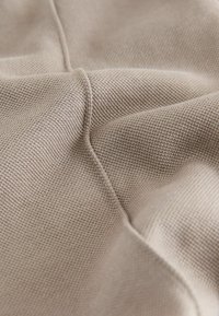 Tissu tissé beige avec une surface texturée. Présente des motifs fins et des plis doux, mettant en valeur un design flexible et léger.