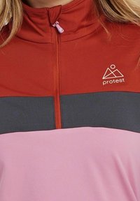 Langärmliges Zip-Up-Oberteil mit hohem Kragen, das rote, graue und rosa Panels aufweist. Texturiertes Material mit kleinem Logo auf der Brust.